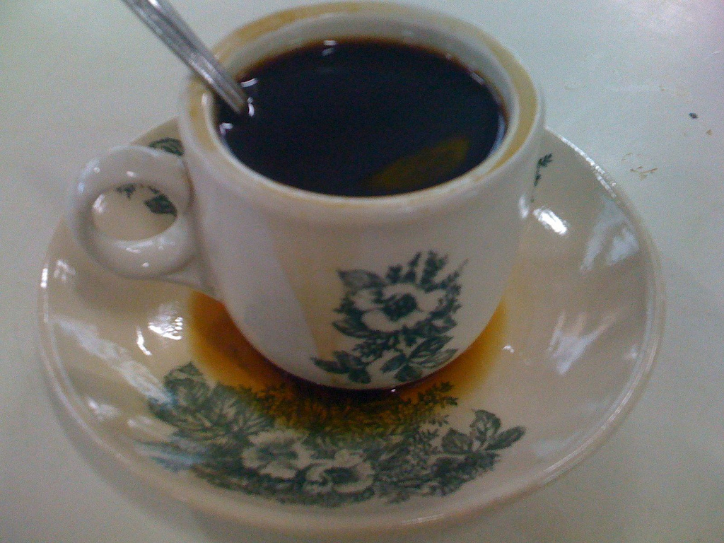 The dedicated photo shows black kopi-o in a traditional cup. It does not show the milk-containing kopi or kopi-c variants.