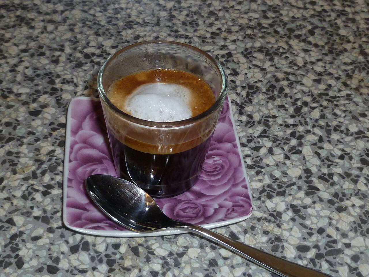 Espresso with a central milk-foam dollop, photographed in a glass. Source photograph documents the drink style, not the named recipe’s measured inputs.