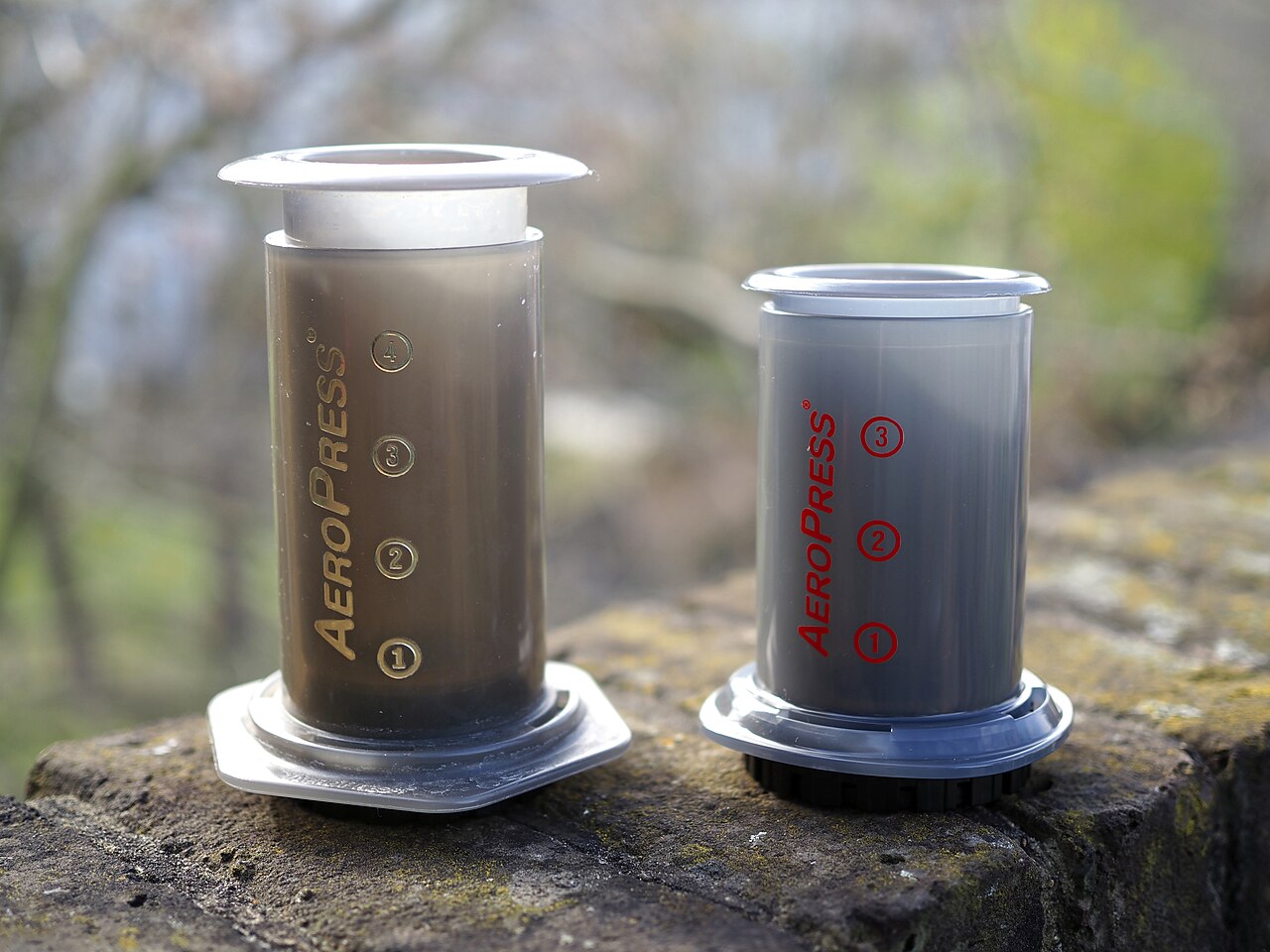 A larger AeroPress on the left and a smaller Go on the right, photographed in 2020. The upright recipe below is a separate Baratza example requiring adequate chamber capacity; do not assume it fits the Go.